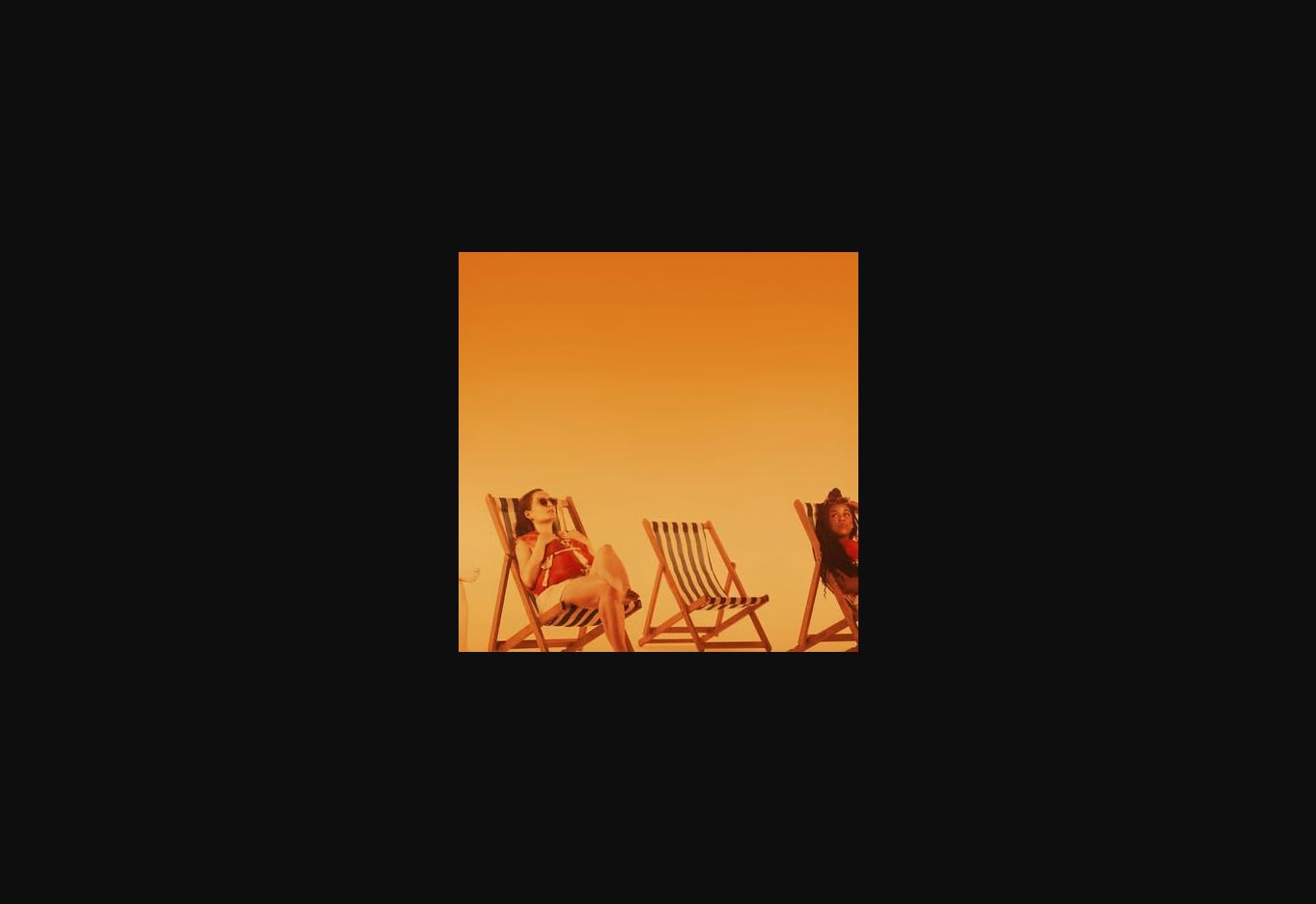 Performers seated on striped deckchairs in warm amber stage light