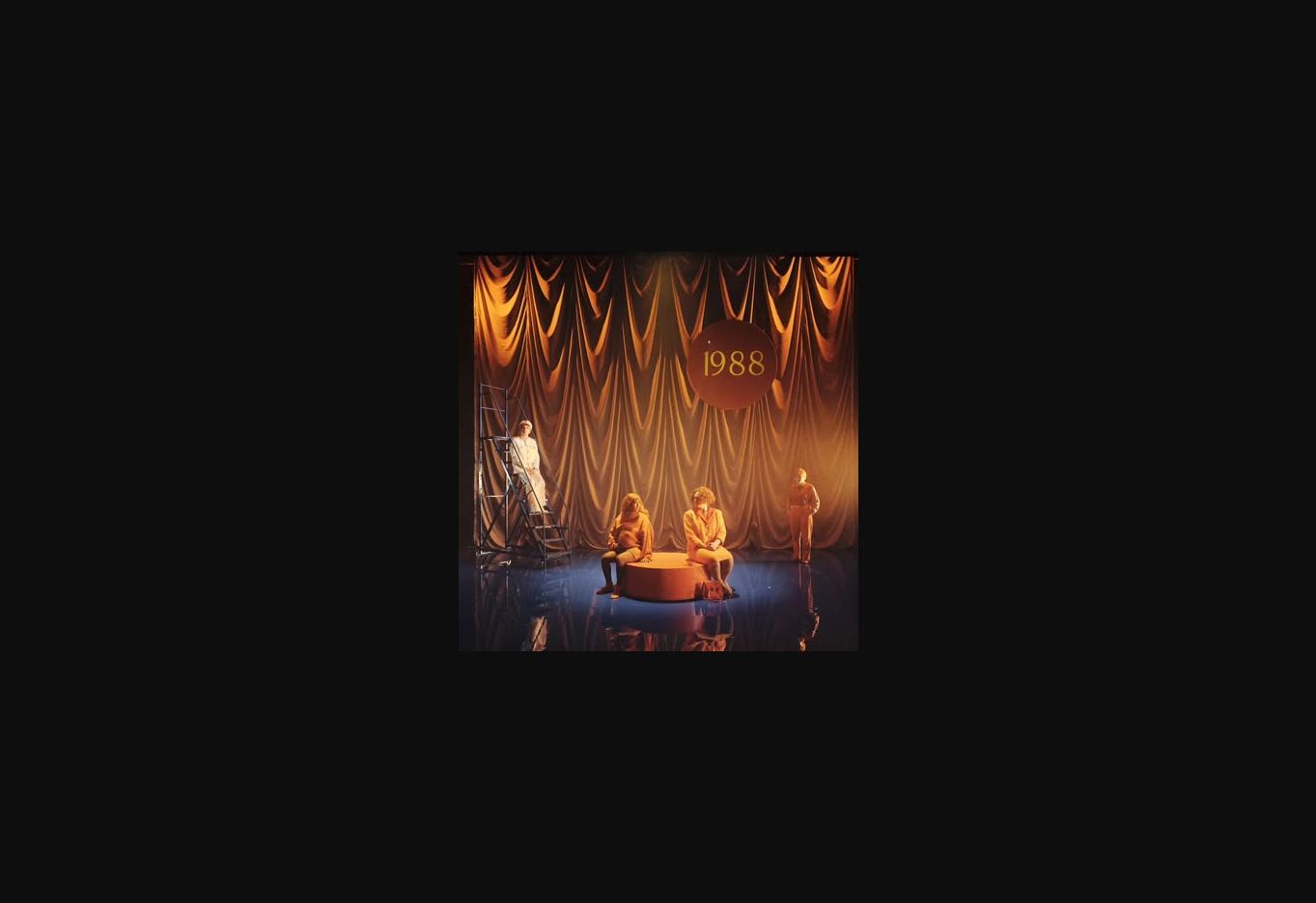 A theatrical stage framed by gold drapery and the year 1988